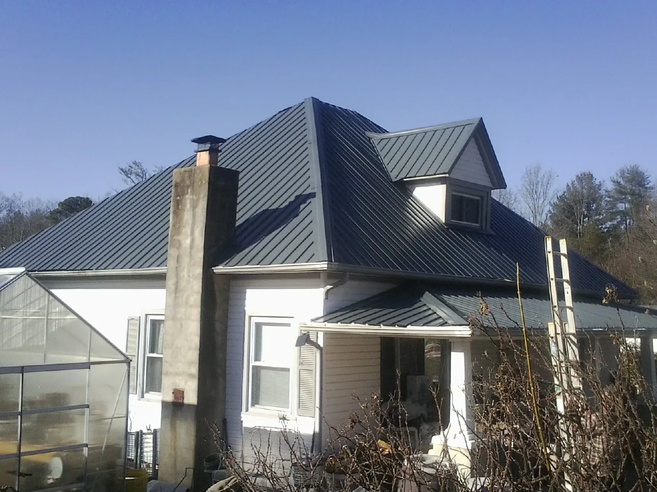 Dark blue standing seam metal roof on a white farmhouse with dormer — Slate & Tile Roof Repair by Roofing Brothers in Gilcrest