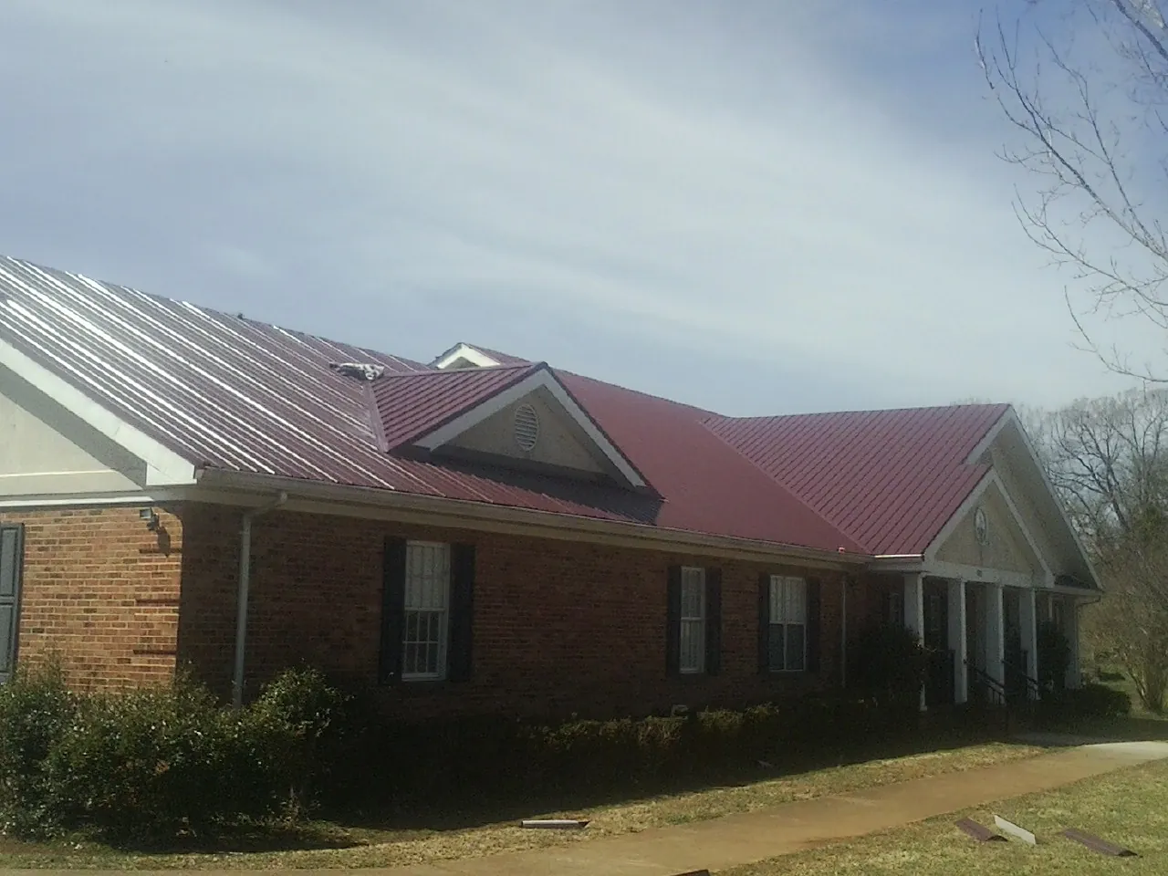 Red metal roof with gabled entries on a long brick building, from a Hail Damage Roof Repair job in Gilcrest