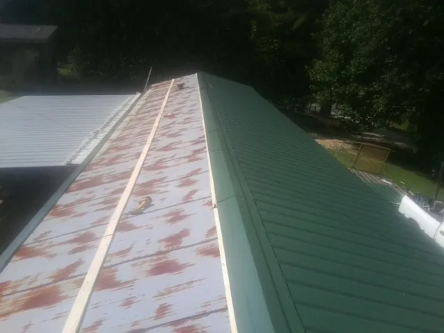Old rusted panels beside newly installed green metal roofing — Wind Damage Roof Repair by Roofing Brothers in Gilcrest