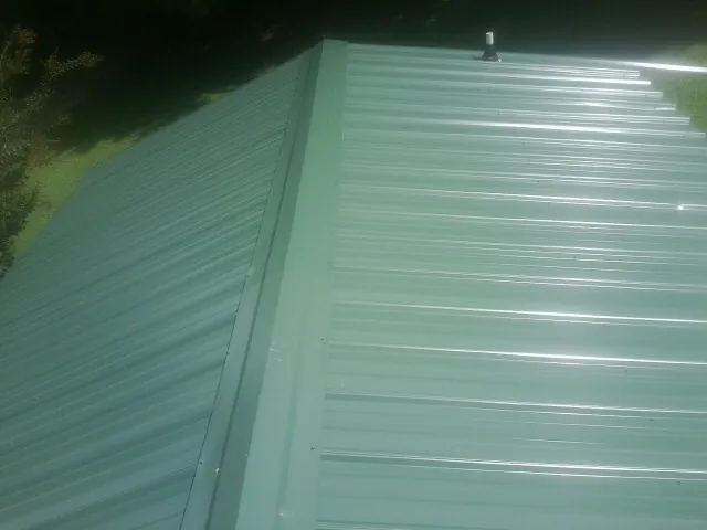 New green metal panels meeting at the ridge of a roof — Flat Roof Repair work by our crew in Gilcrest