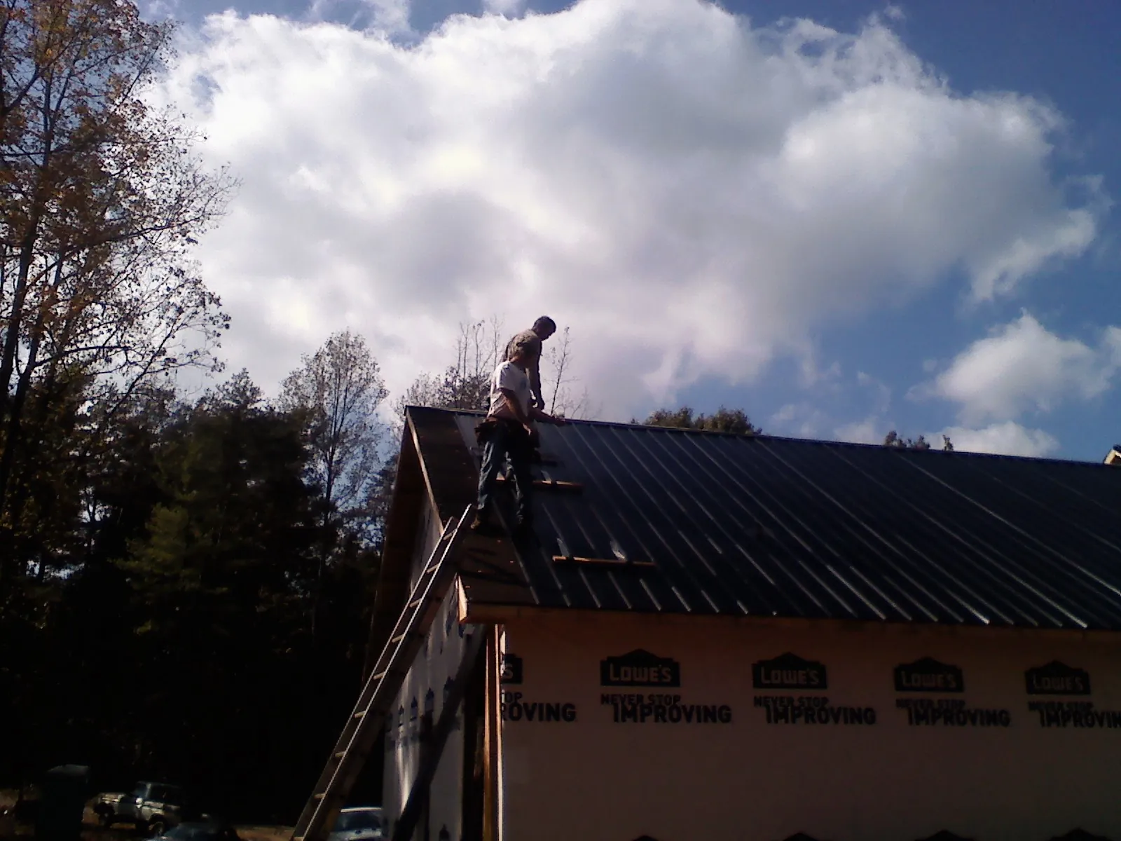 Roofer fastening dark metal panels high against a cloudy sky in Gilcrest