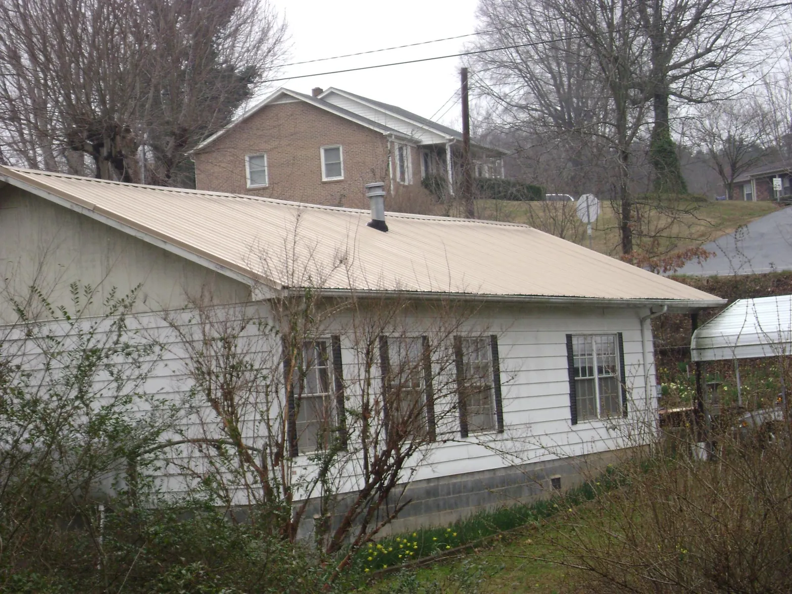 Tan metal roof on a white sided house set into a hillside — Commercial Roofing by Roofing Brothers in Gilcrest