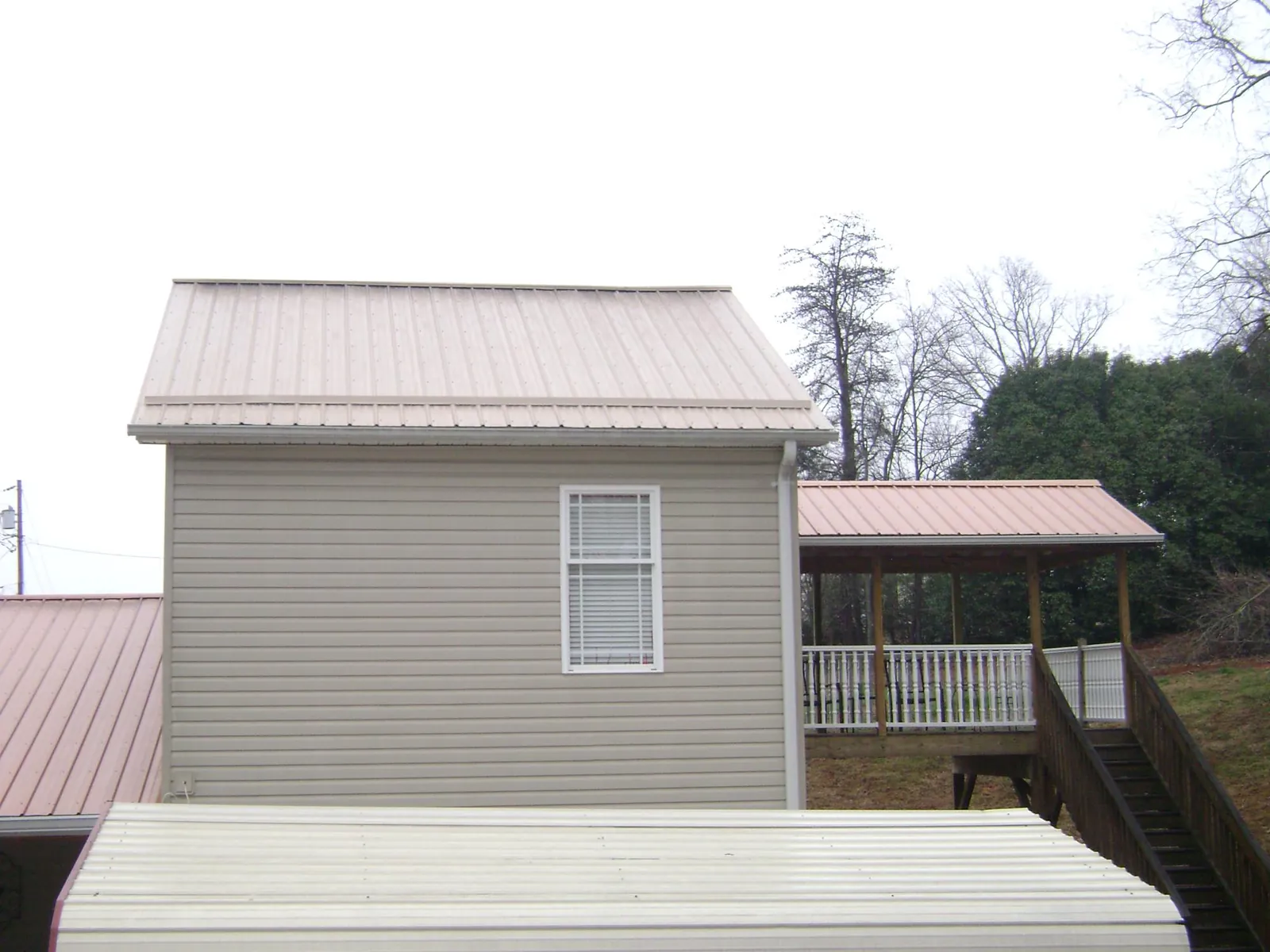 Tan metal roofs on a two story addition and attached porch, from a Roof Replacement job in Gilcrest
